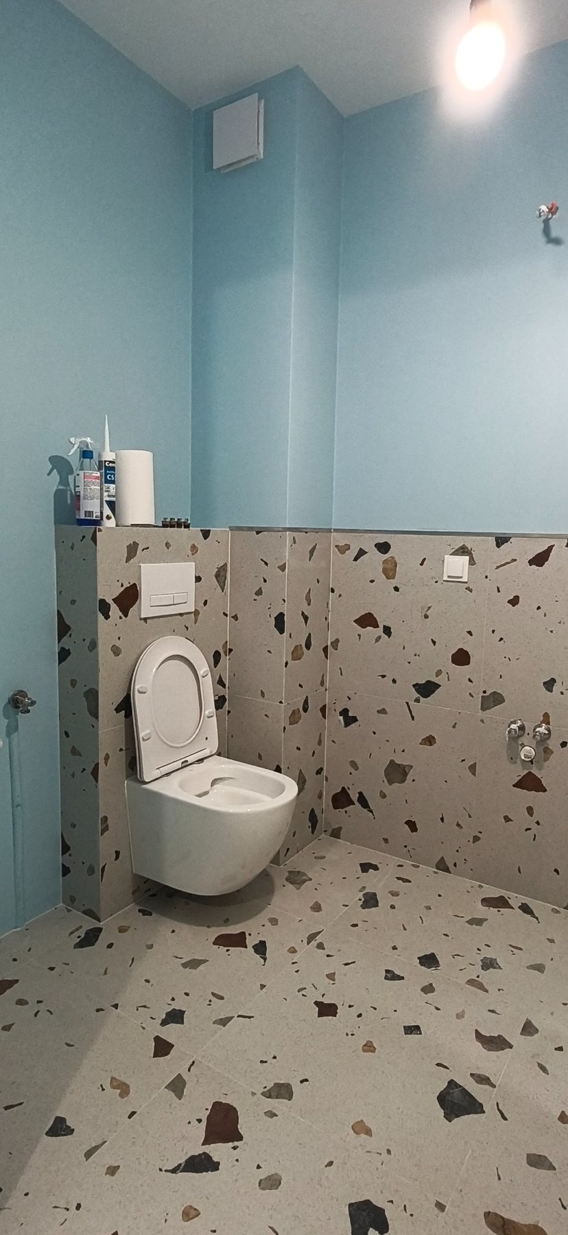 Zabudowa stelaża WC, płytki lastryko i jasnoniebieskie ściany w łazience